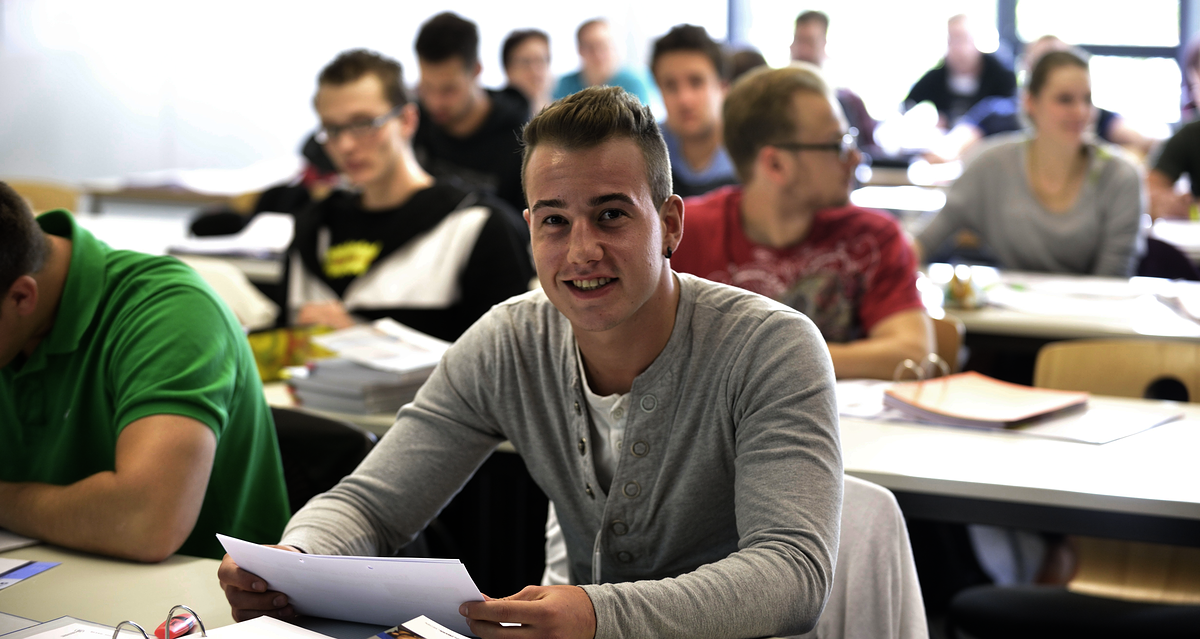 Meisterausbildung Tischreihen, hintereinander, erste Reihe, Teilnehmer Blick vorne, lächelt, Hintergrund unscharf, Bachelorstudiengang_Unternehmensführung_15585_argum