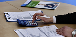 Nahaufnahme von Hand, Taschenrechner, Tisch mit Tabellen und Broschüre, Finanzierung_FH54261_argum