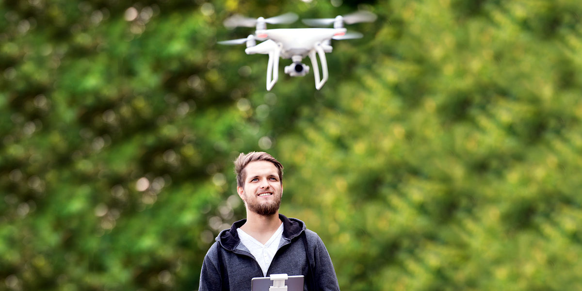 Young hipster man with remote control and flying drone with camera. Green sunny nature. Schlagwort(e): drone, quadrocopter, white, isometric, camera, aircraft, air, technology, fly, vehicle, aviation, 3d, digital, modern, future, flight, control, wireless, aerial, propeller, spy, action, flying, motion, helicopter, quadcopter, professional, man, equipment, remote, hipster, beard, mustache, remote control, tablet, device, gadget, nature, green, sunny, sunlight, tree, forest, summer, sweatshirt, landing gear, filming, take photo, take picture, drone, quadrocopter, white, isometric, camera, aircraft, air, technology, fly, vehicle, aviation, 3d, digital, modern, future, flight, control, wireless, aerial, propeller, spy, action, flying, motion, helicopter, quadcopter, professional, man, equipment, remote, hipster, beard, mustache, remote control, tablet, device, gadget, nature, green, sunny, sunlight, tree, forest, summer, sweatshirt, landing gear, filming, take photo, take picture