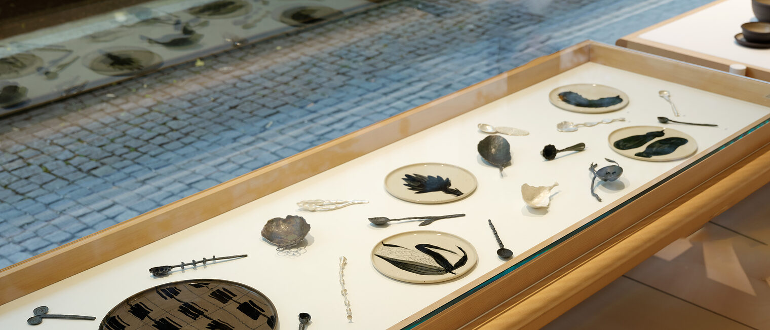 Teller und Besteck Schaukasten mit handgefertigtem, filigranem Besteck und kleinen Tellern mit unterschiedlichen abstrakten Motiven.