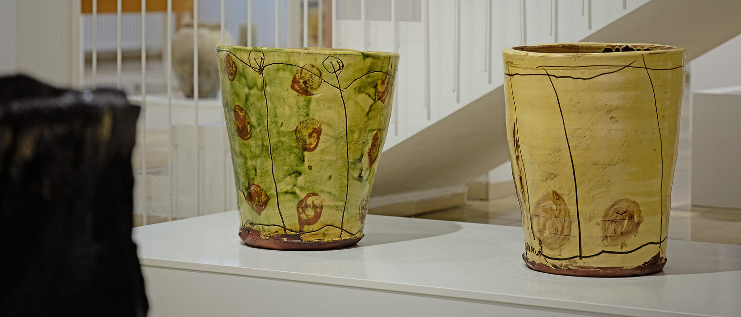 Zwei große Blumentoepfe bemalt mit gedeckten Farben, gruen-braun und pastell-gelb mit braunen herbstlichen Blaettern 