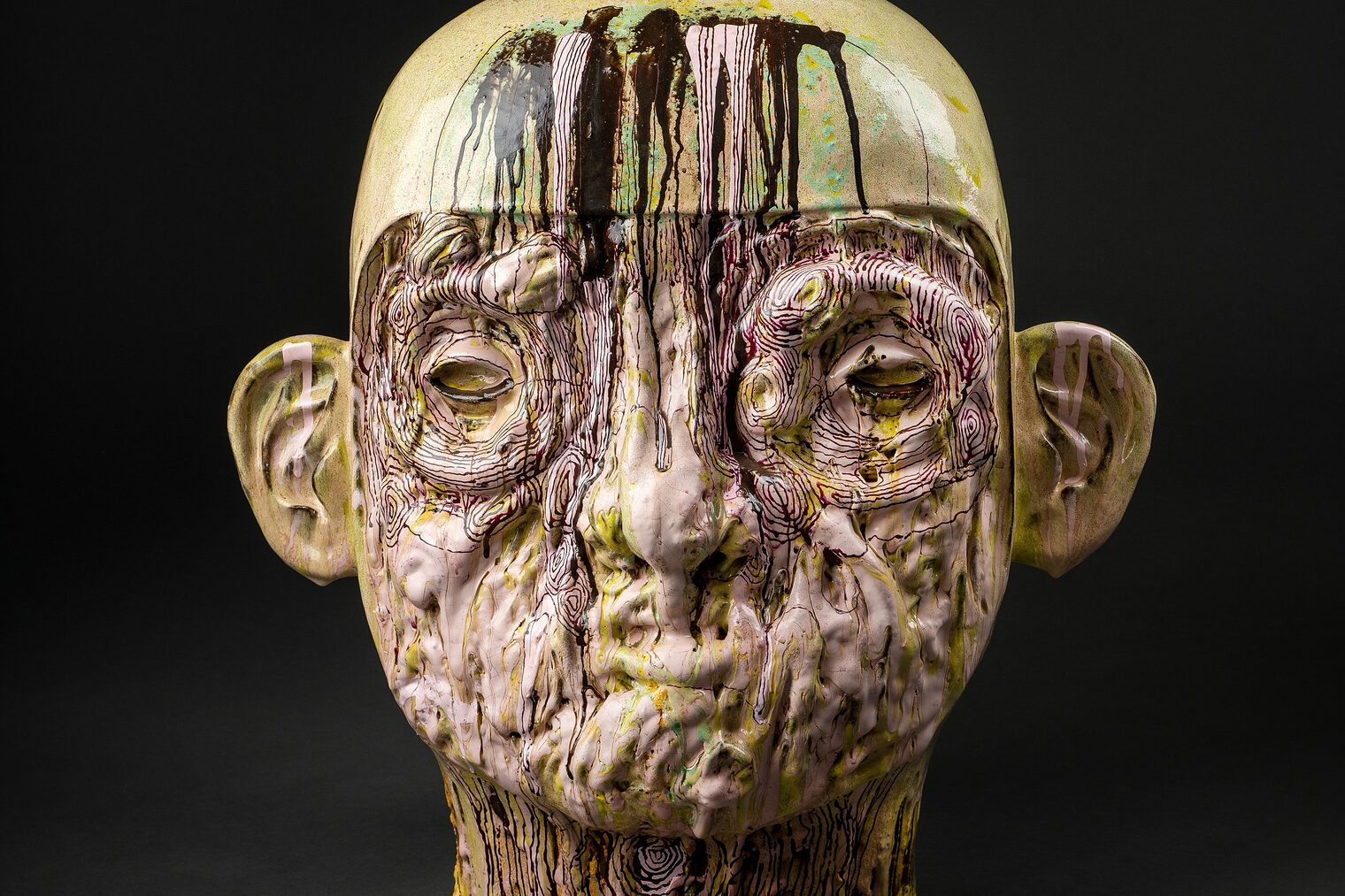 Hautfarbener, mit hellgrünen Schlieren durchzogener Männerkopf mit filigranem braunem Linienmuster aus Keramik