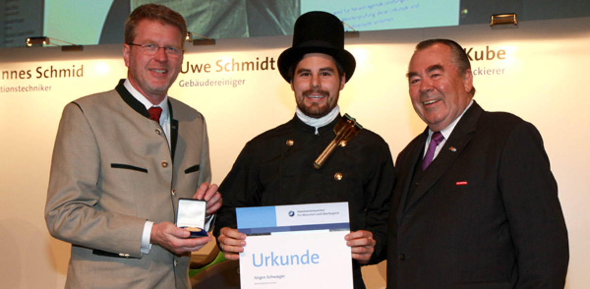 Handwerkskammerpräsident Heinrich Traublinger, MdL a. D. (rechts) und Umweltminister Dr. Marcel Huber, MdL (links) überreichten Kaminkehrermeister Jürgen Schwaiger seine Urkunde als Jahresbestmeister.